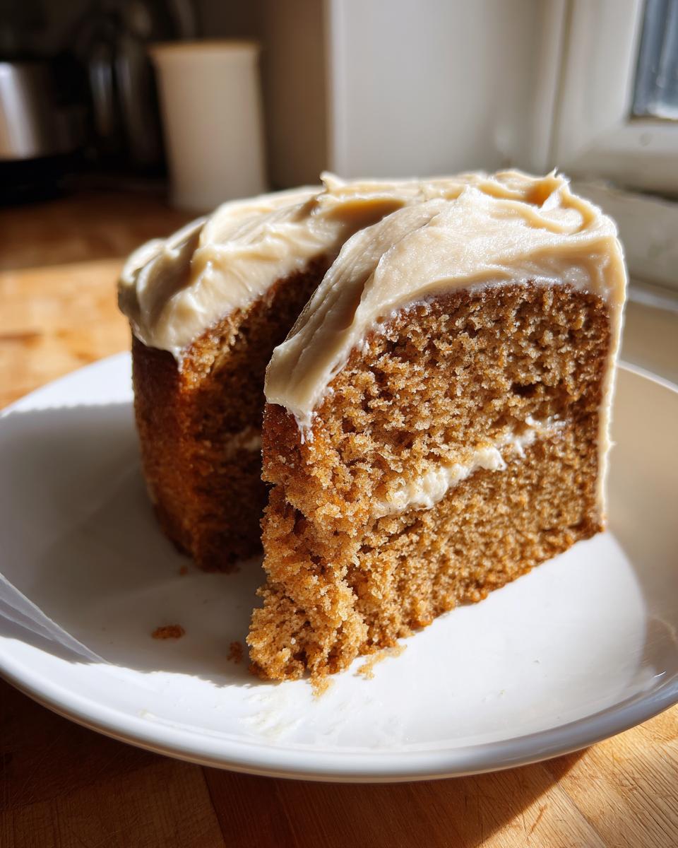 Two slices of moist, spiced applesauce cake topped with thick, creamy frosting on a white plate.
