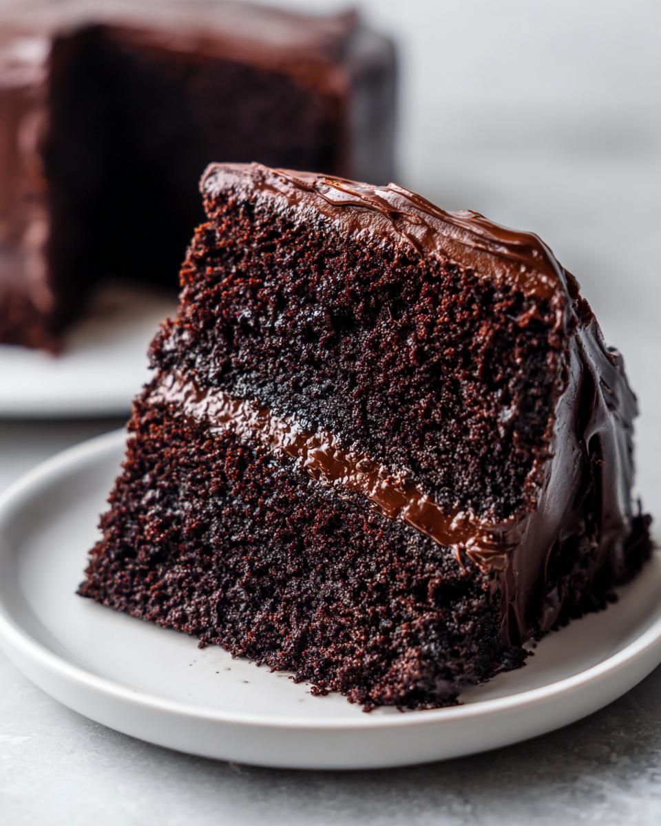 Close-up of a perfect slice of moist chocolate cake showing its dark, rich crumb and thick fudge frosting.