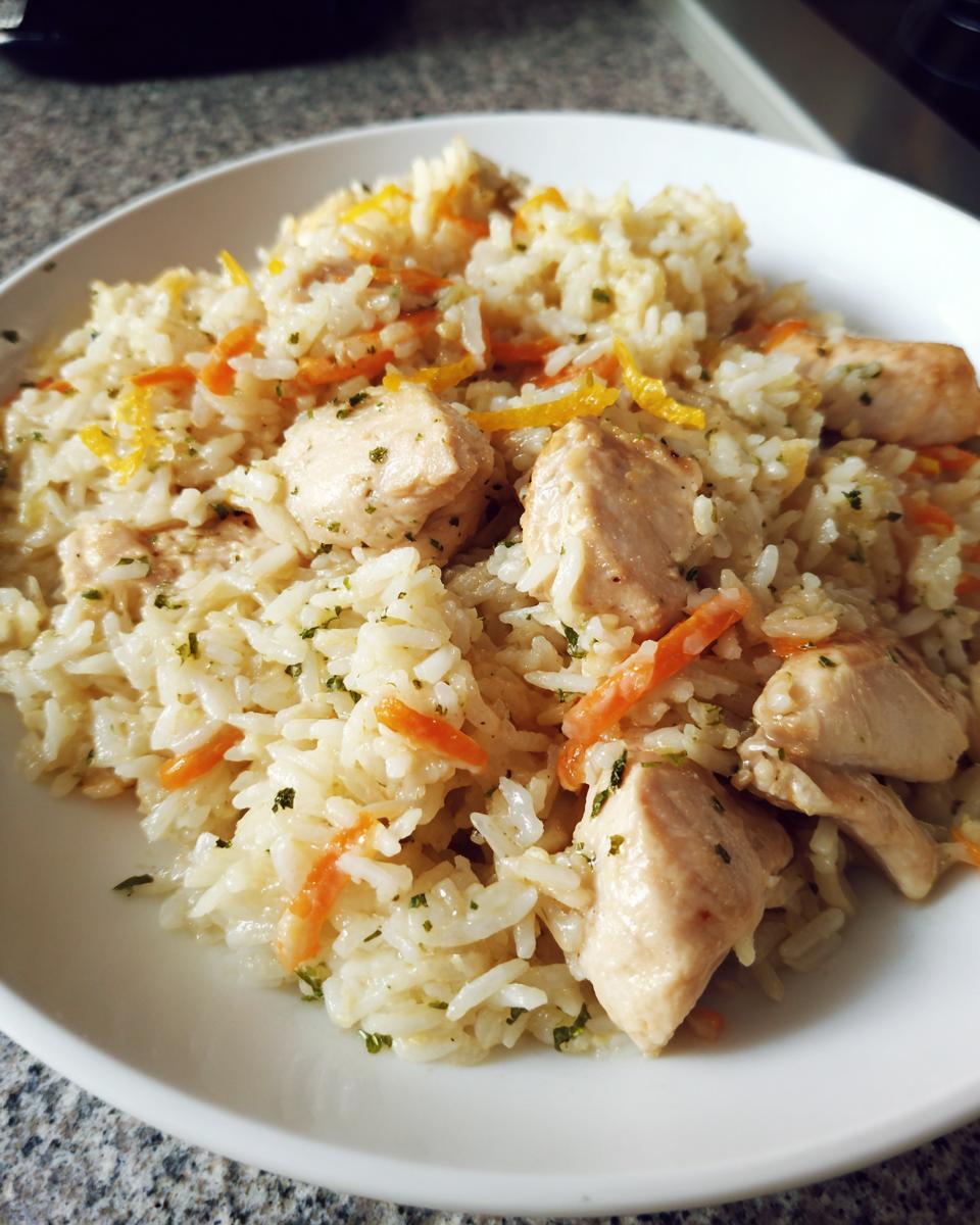 Close-up of a white plate filled with moist one pot chicken and rice mixed with shredded carrots and herbs.