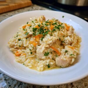 Close-up of a white bowl filled with creamy one pot chicken and rice, topped with chopped carrots and parsley.