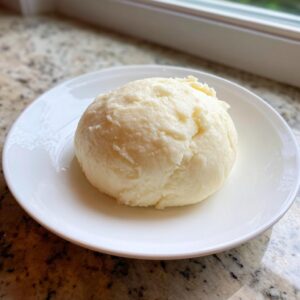 A smooth, light-colored ball of freshly made fufu served on a small white plate.