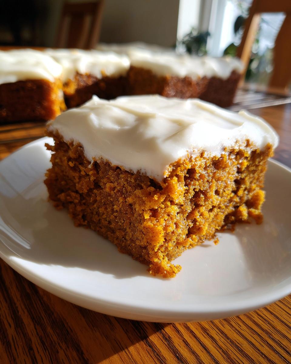 Close-up of a moist slice of pumpkin bars with cream cheese frosting on a white plate.