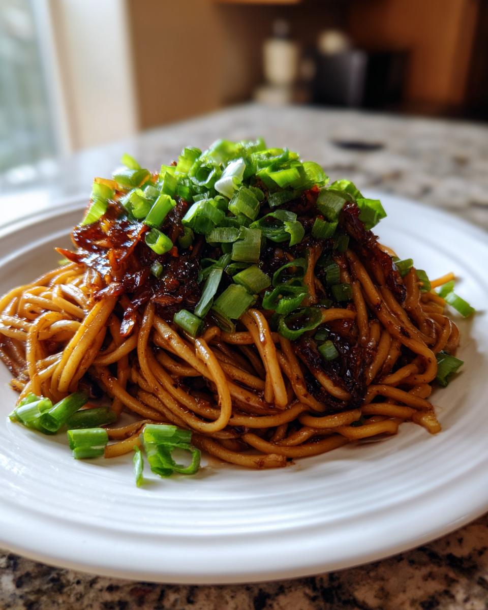 A close-up of savory garlic noodles tossed in a dark sauce and topped generously with fresh chopped green onions.