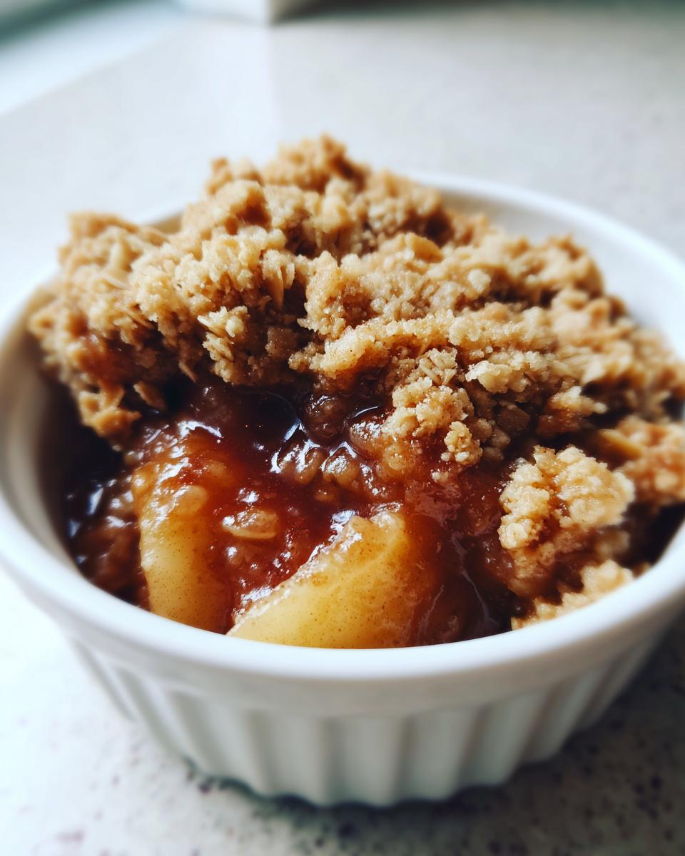 Close-up of a single serving of apple crisp recipe in a white ramekin, showing gooey apples and crunchy topping.