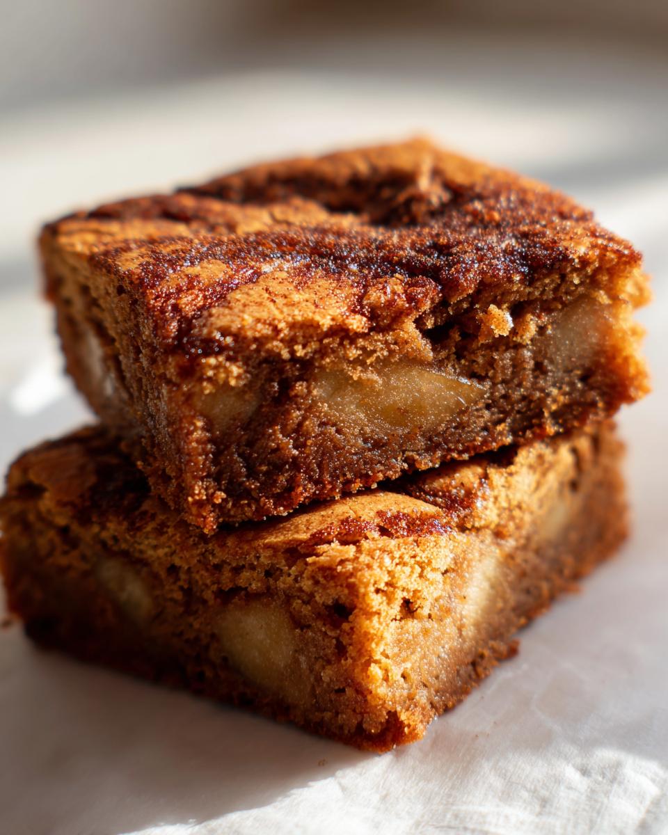 Close-up of two stacked, moist apple brownies showing chunks of apple inside and a cinnamon swirl topping.