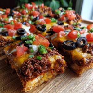 Close-up of thick slices of amazing mexican pizza topped with seasoned ground beef, melted cheese, black olives, tomatoes, and green onions.