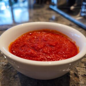 Close-up of a small white bowl filled with rich, bright red homemade pizza sauce.