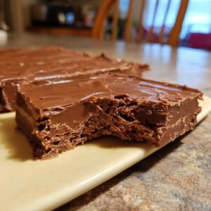 A close-up shot of a rich, smooth piece of chocolate fudge with a bite taken out, showing its texture.