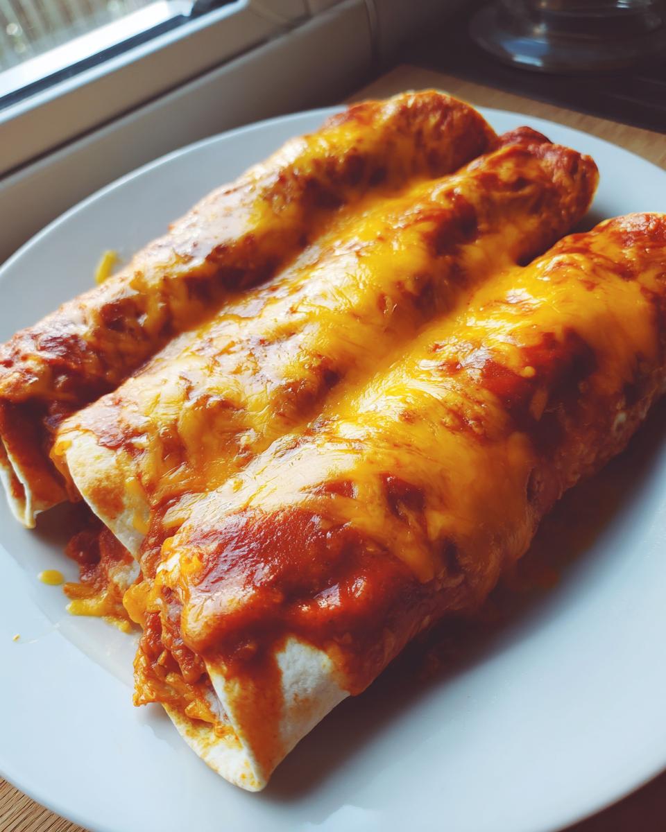 Three baked cheese enchiladas covered in rich red sauce and melted orange cheddar cheese on a white plate.