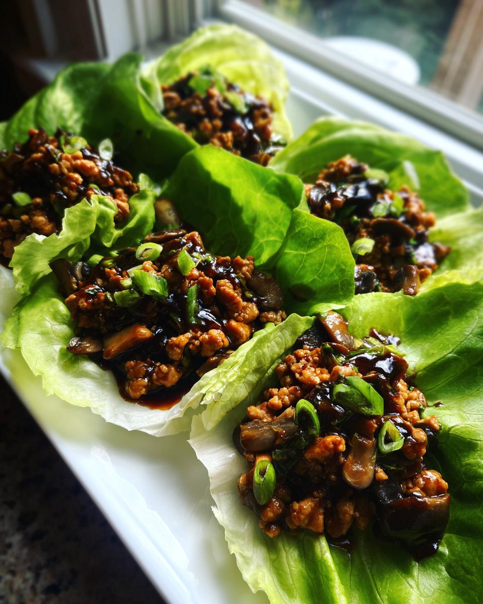 Close-up of four servings of amazing chicken lettuce wraps filled with savory ground chicken and mushrooms, topped with green onions.