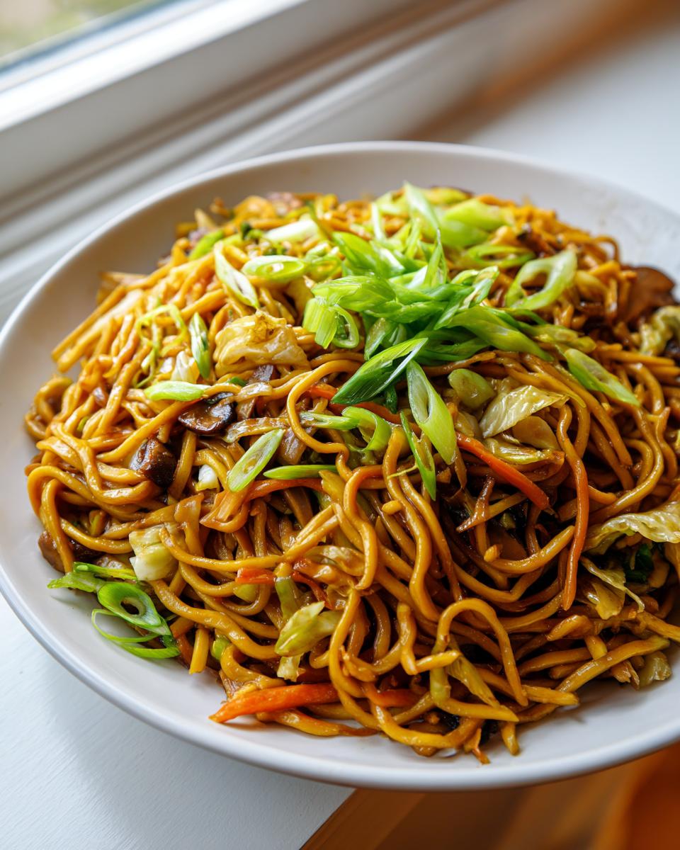 A close-up of a white bowl filled with savory, saucy fried noodles topped with fresh green onions.