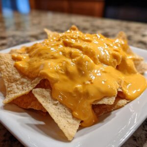 Close-up of tortilla chips generously covered with thick, bright orange nacho cheese sauce on a white plate.