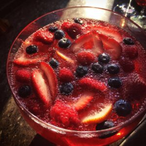 Close-up of a bright red champagne punch filled with floating strawberries, blueberries, and raspberries.