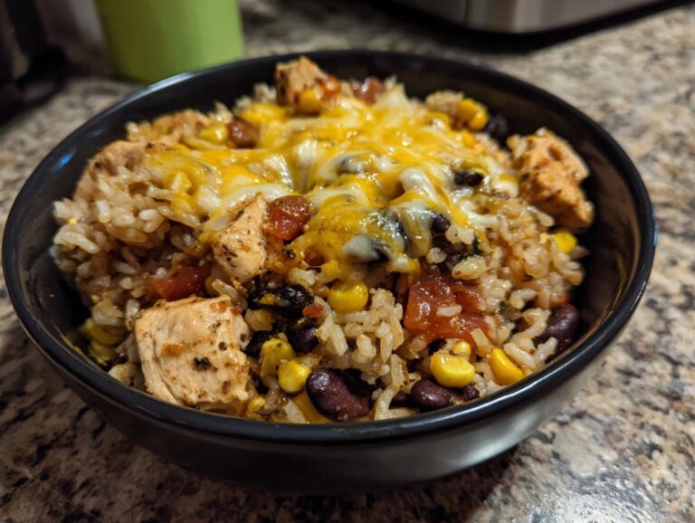 Close-up of a black bowl filled with a delicious chicken burrito bowl featuring seasoned rice, black beans, corn, tomatoes, and melted cheddar cheese.