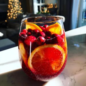 Close-up of a glass filled with sparkling Christmas sangria, garnished with bright orange slices and whole cranberries.