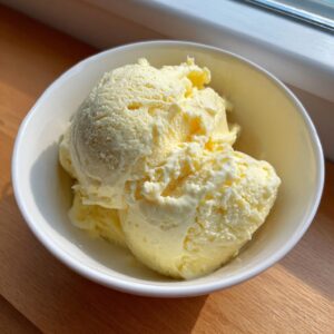 Three scoops of pale yellow, creamy banana ice cream served in a white bowl.