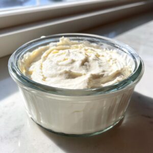A small glass bowl filled with thick, creamy horseradish sauce, lit by natural sunlight.