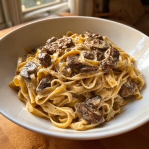 Close-up of creamy fettuccine mushroom pasta generously topped with sautéed mushrooms and black pepper in a white bowl.