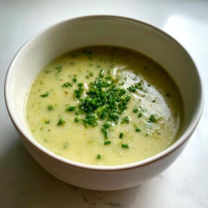 A close-up of a bowl of creamy, pale green potato leek soup garnished generously with chopped fresh chives.