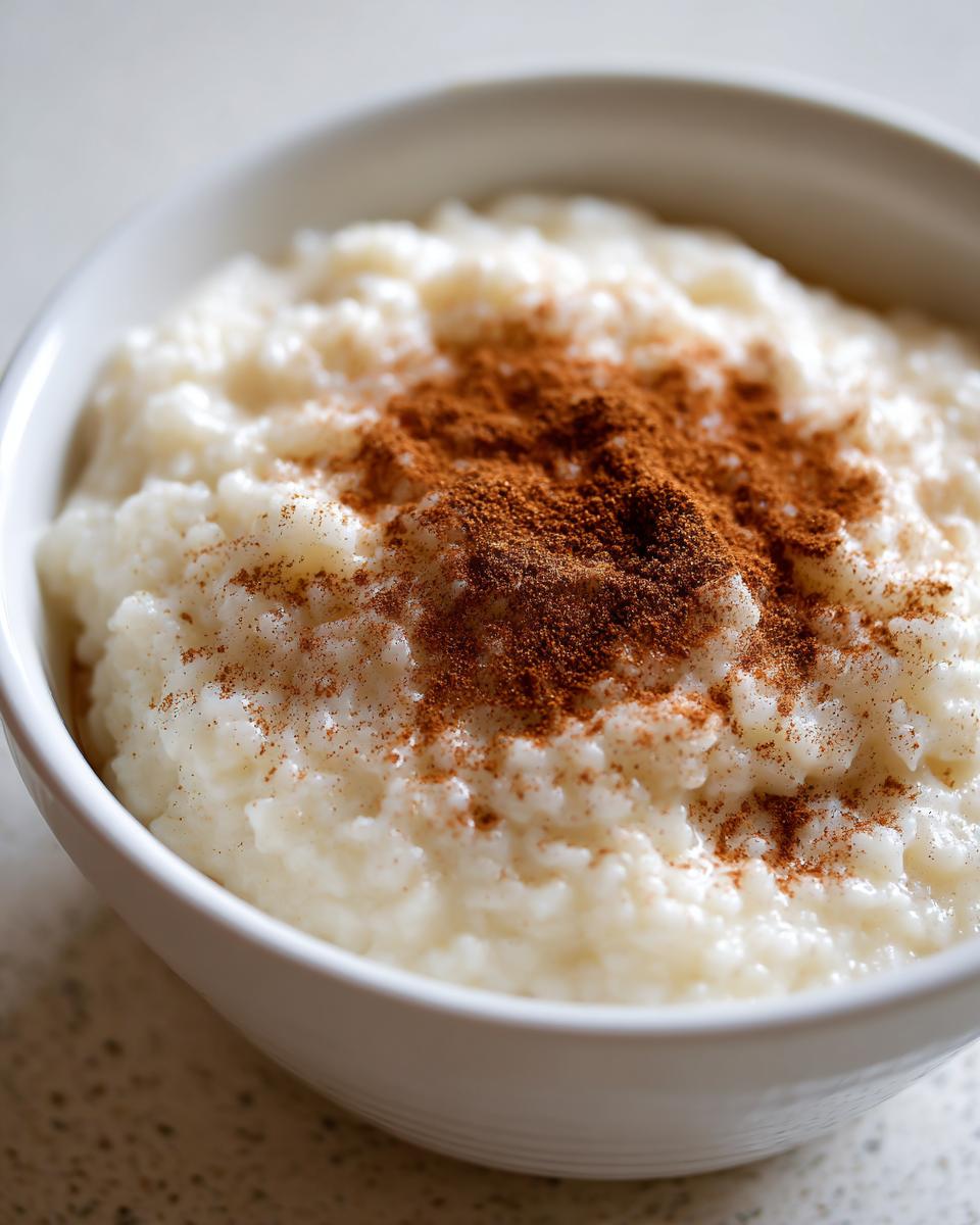 Close-up of a white bowl filled with creamy rice pudding generously dusted with ground cinnamon.