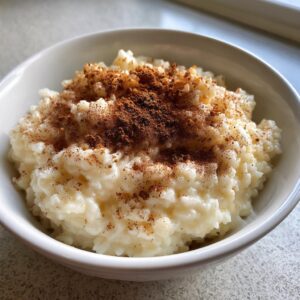 A close-up of creamy rice pudding topped generously with ground cinnamon in a white bowl.