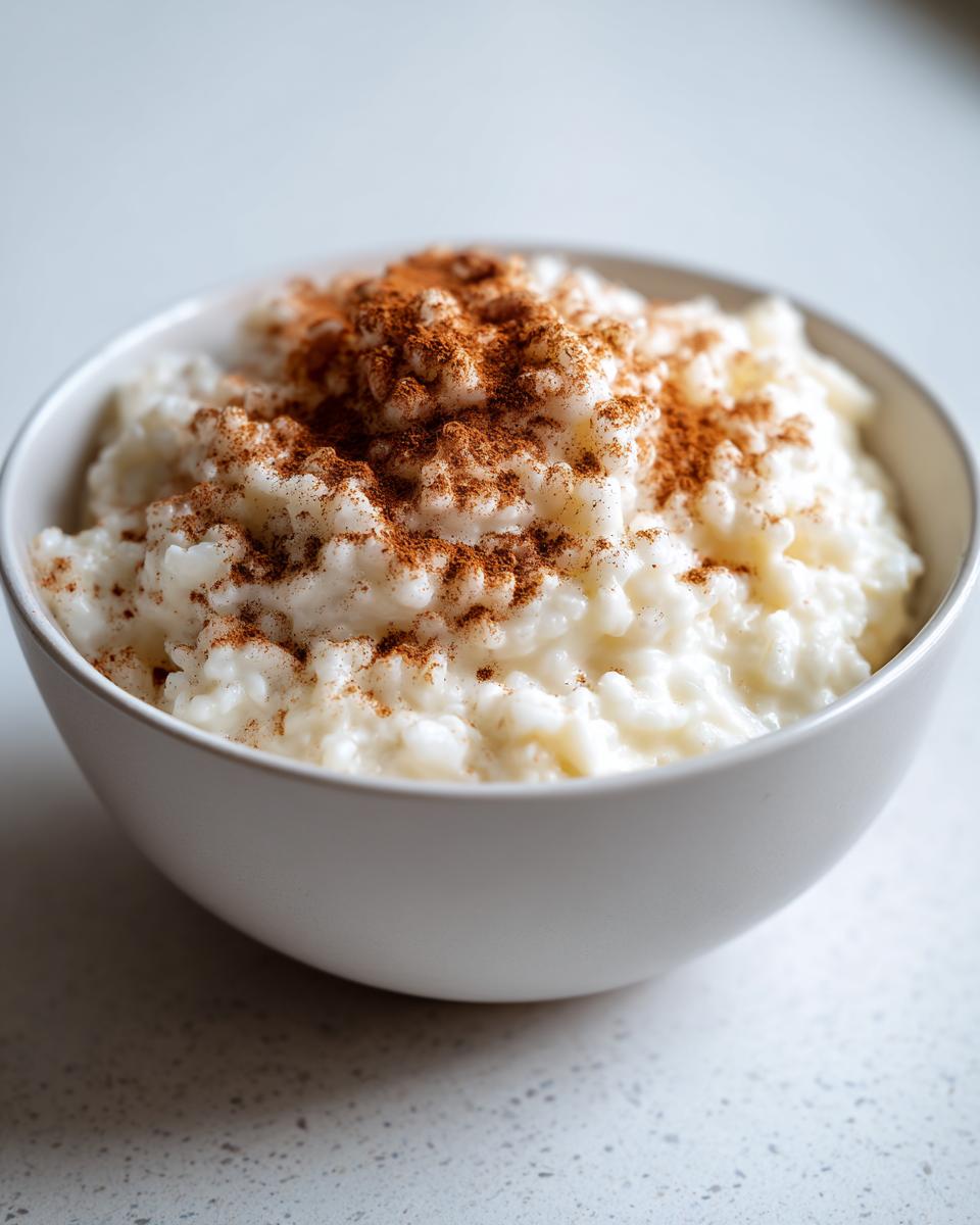 A close-up of creamy rice pudding in a white bowl, generously dusted with ground cinnamon.