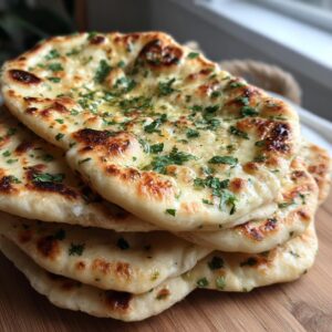 A close-up stack of freshly made, fluffy naan bread brushed with melted butter and topped with chopped parsley.