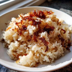 A close-up of fluffy french onion butter rice topped generously with dark, crispy fried onions in a white bowl.
