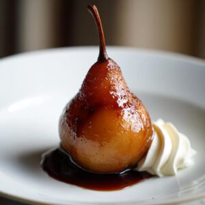 A single, glossy poached pear served on a white plate with a dollop of whipped cream and dark syrup.