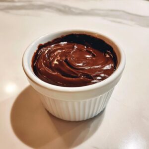 A close-up of rich, dark homemade chocolate pudding swirled in a small white ramekin.