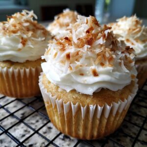 Close-up of moist coconut cupcakes topped with white frosting and toasted coconut flakes.