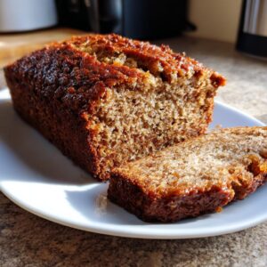 A close-up of a moist sourdough banana bread loaf, partially sliced, showing its rich brown crust and soft crumb.