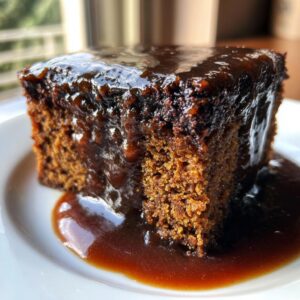 Close-up of a rich, dark slice of sticky toffee pudding recipe covered in glossy toffee sauce.