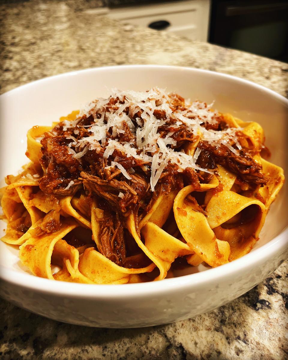 A bowl of wide pappardelle pasta topped generously with rich beef ragu and grated Parmesan cheese.