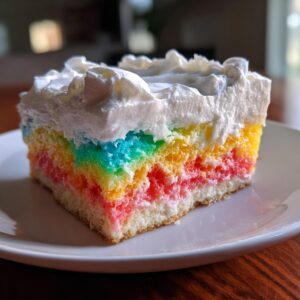 A vibrant slice of rainbow jello poke cake topped with fluffy white whipped cream, served on a white plate.