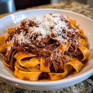 A close-up of wide pappardelle pasta generously topped with rich, shredded beef ragu and grated Parmesan cheese.