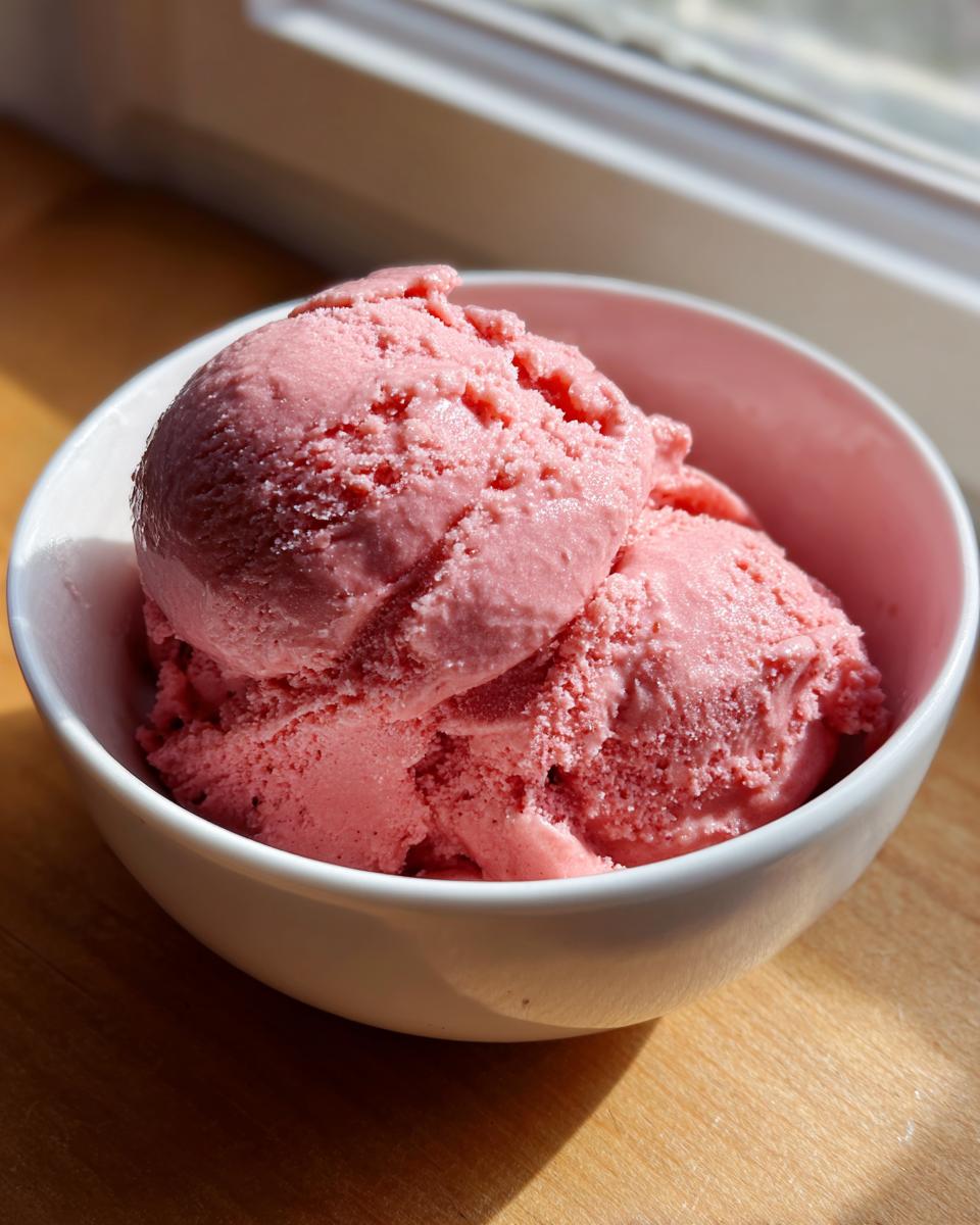 Three scoops of vibrant pink strawberry ice cream served in a small white bowl, brightly lit by sunlight.