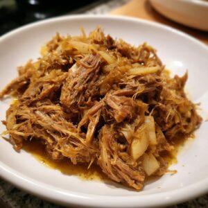 Close-up of tender, shredded pork and sauerkraut mixture served in a white bowl.