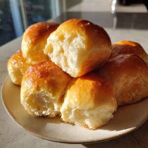 A stack of golden brown, fluffy sourdough discard rolls piled on a light plate.