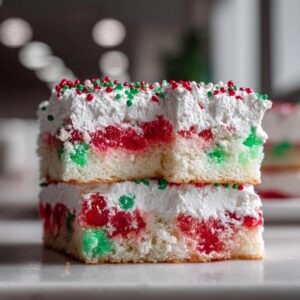 Two stacked slices of a moist christmas poke cake featuring red and green gelatin pockets and white whipped topping.
