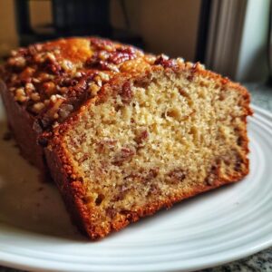 Close-up of a slice of moist sweet Alabama pecan bread showing pecans throughout the crumb, served on a white plate.