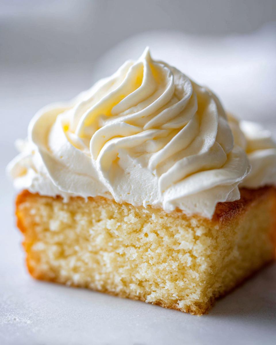 Close-up of a square slice of yellow cake generously topped with perfectly piped vanilla buttercream.