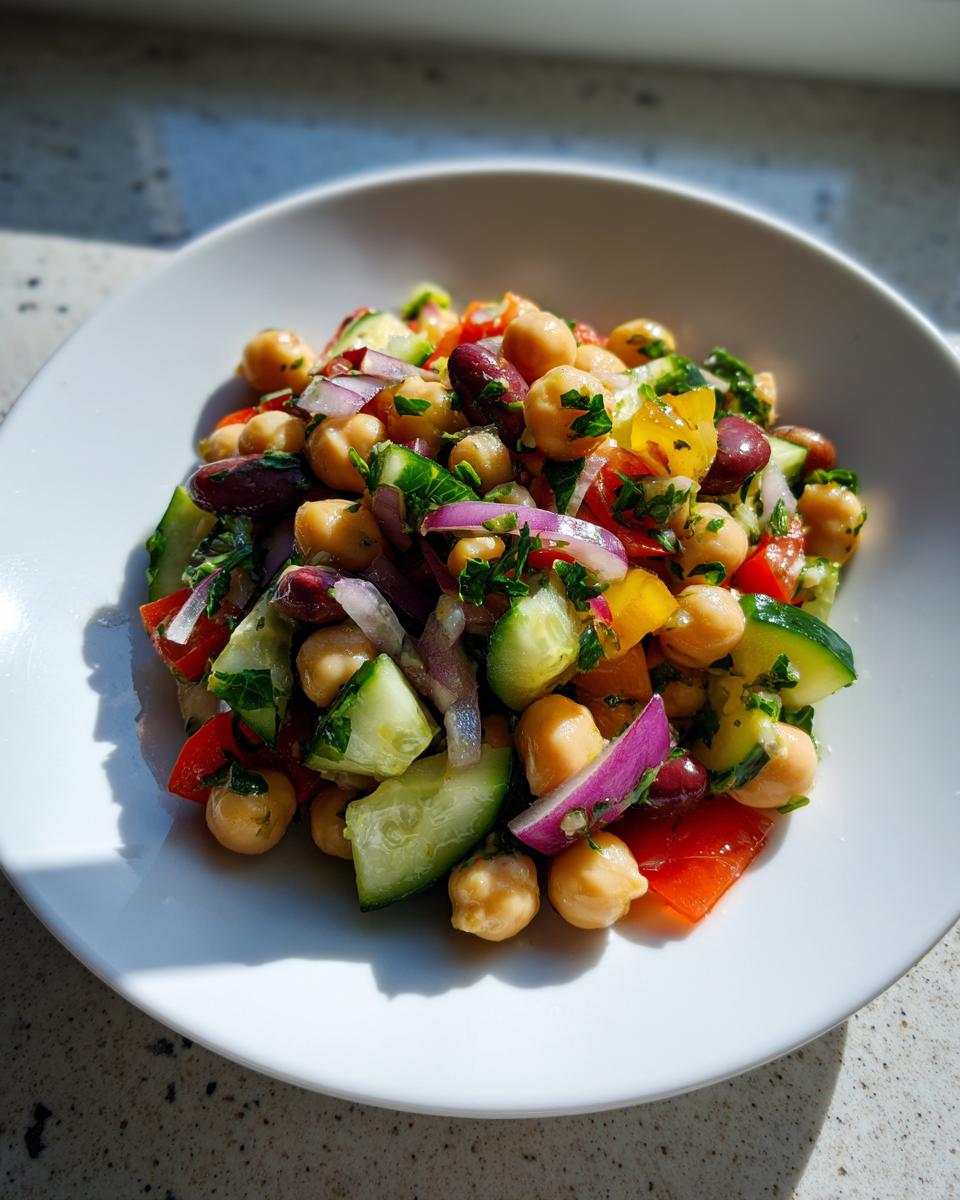 A vibrant serving of fresh bean salad featuring chickpeas, kidney beans, cucumber, red onion, and bell peppers.