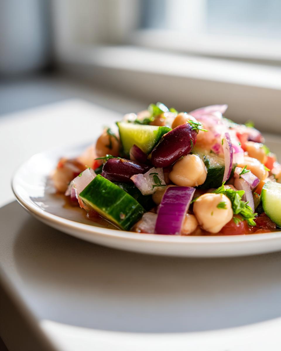 Close-up of a colorful bean salad featuring chickpeas, kidney beans, cucumber, and red onion, dressed lightly.